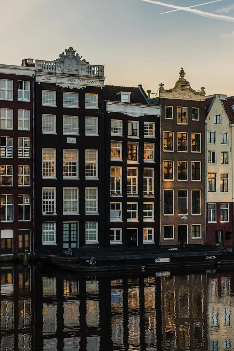 Scenic view of iconic canal houses in Amsterdam with reflections in the water during sunset.