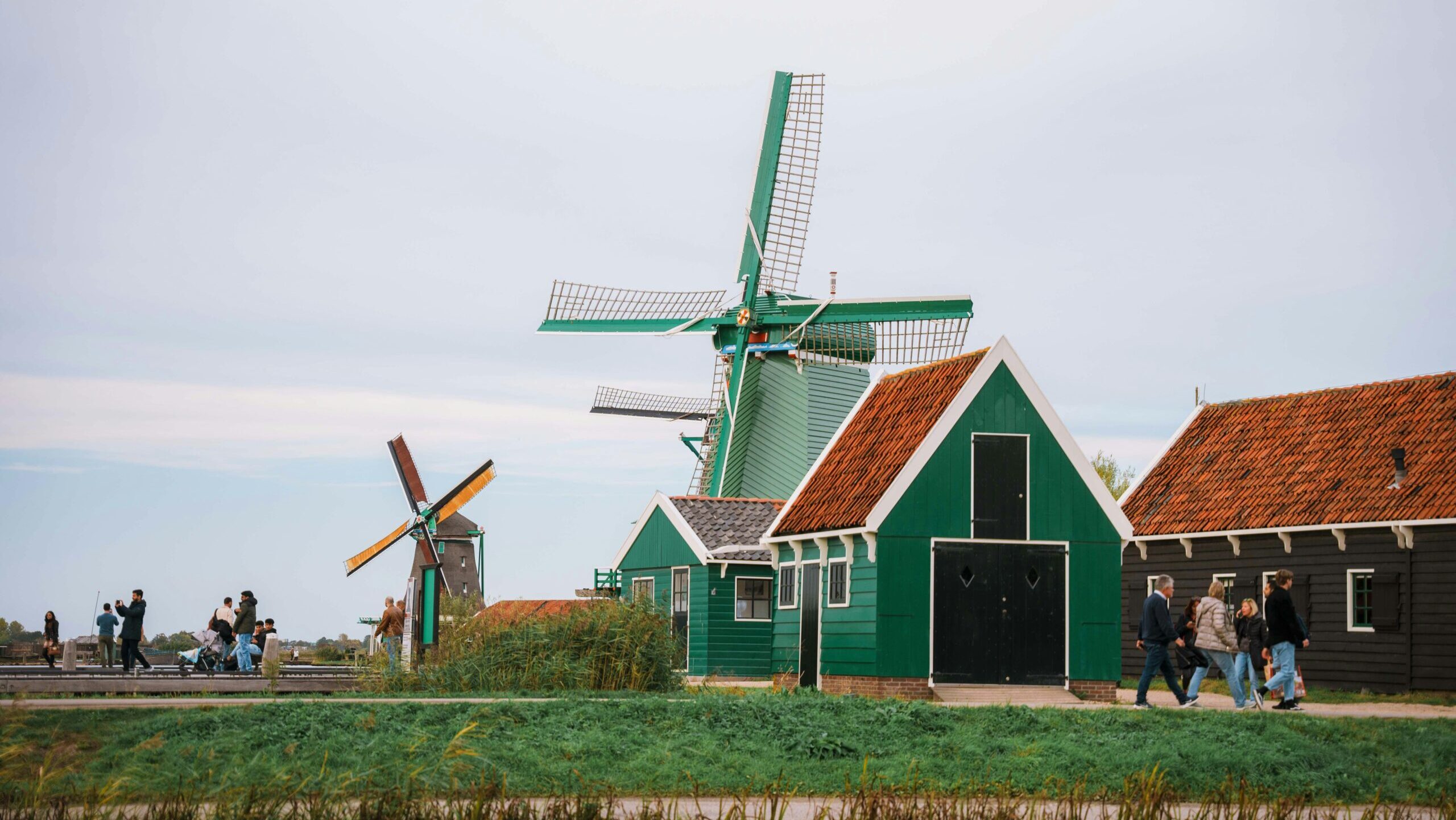 Countryside scene with traditional Dutch windmills and people walking nearby.