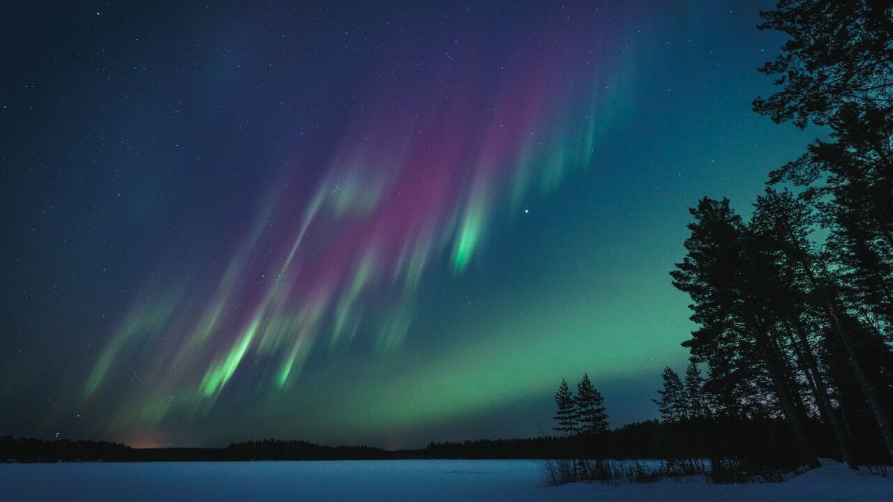 Northern lights illuminate the night sky over a serene lake in Oulu, Finland.