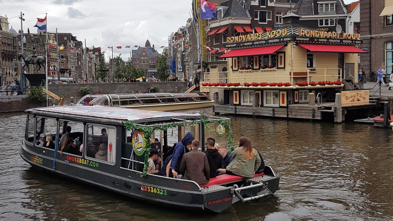 People enjoying a canal cruise in Amsterdam with iconic Dutch architecture in the backdrop.
