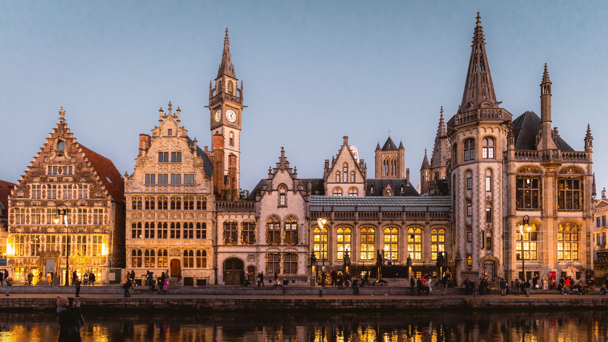 Beautiful medieval buildings in Ghent illuminated at twilight along a reflective canal.