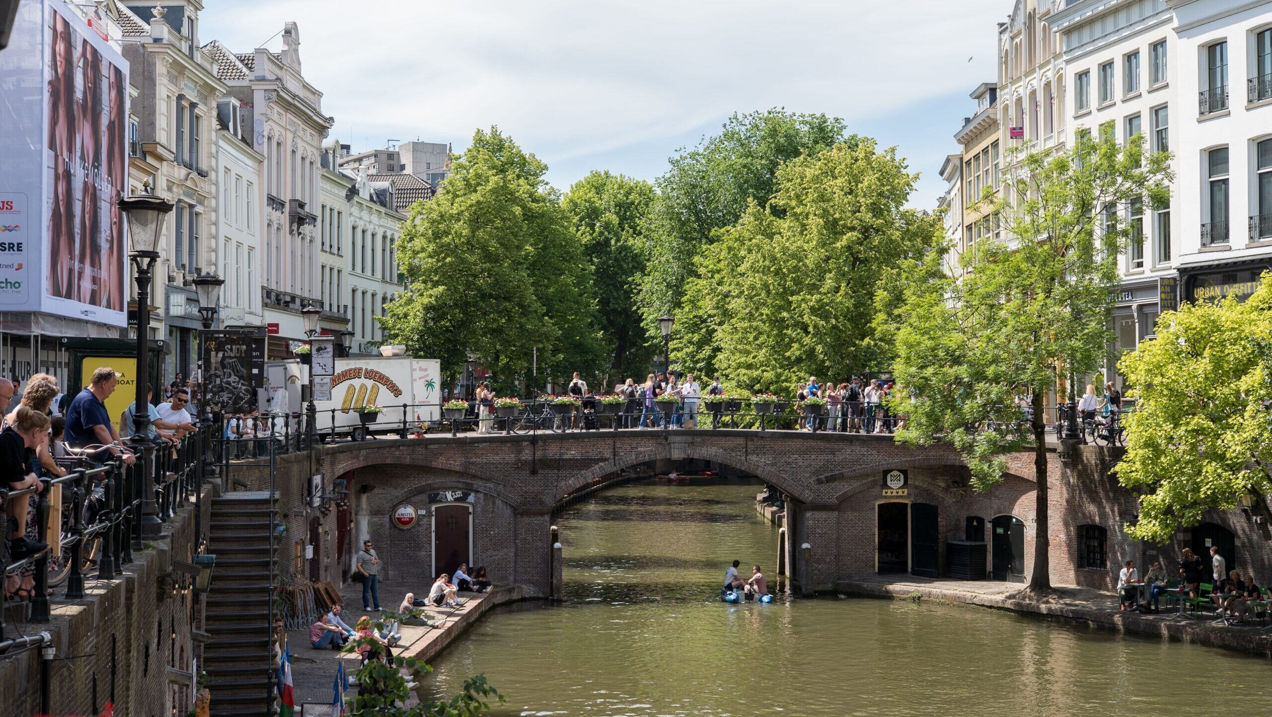 Charming canal with busy bridge in Utrecht, Netherlands, showcasing summer urban life.